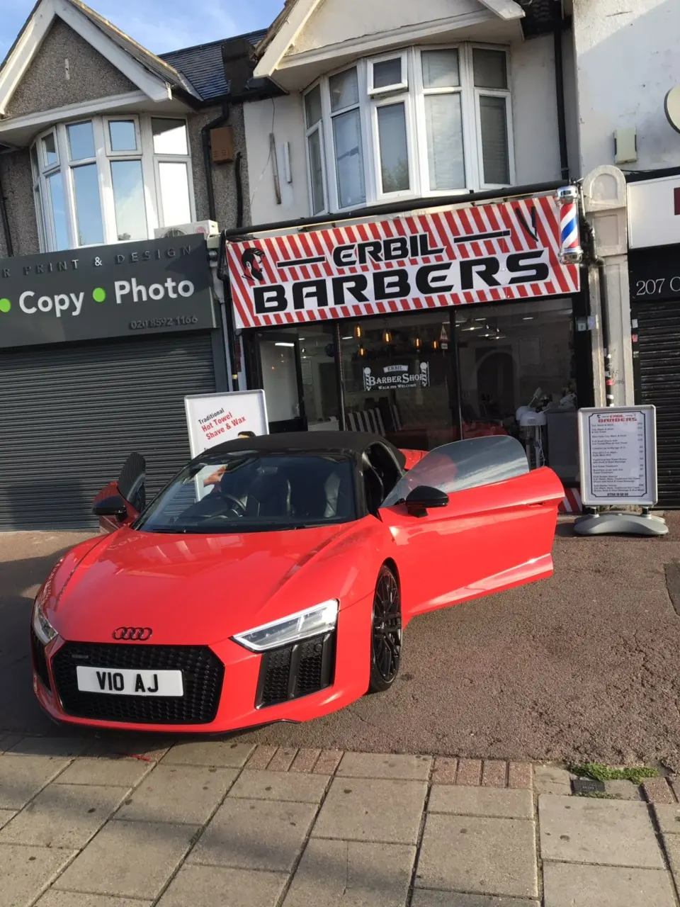A red sports car parked outside under the BARBERS sign