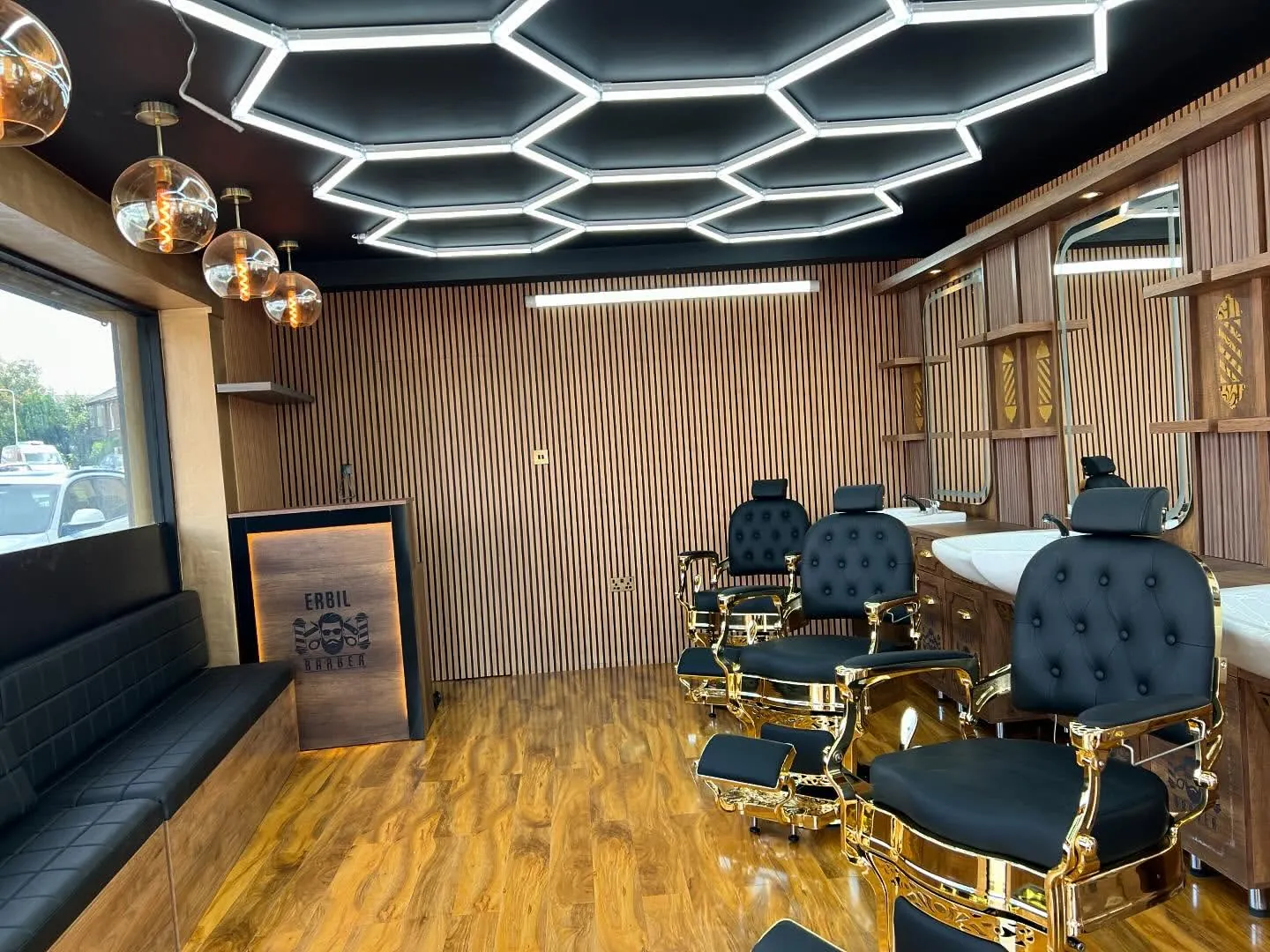 Inside Erbil Barbers: black and gold chairs, wood-slat walls, the ERBIL counter and a hexagon light ceiling